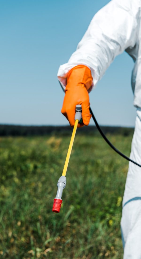 cropped view of exterminator in orange latex glove and white uniform holding spray outside