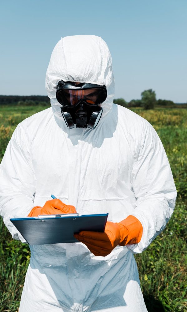 exterminator in protective mask and uniform writing while holding clipboard